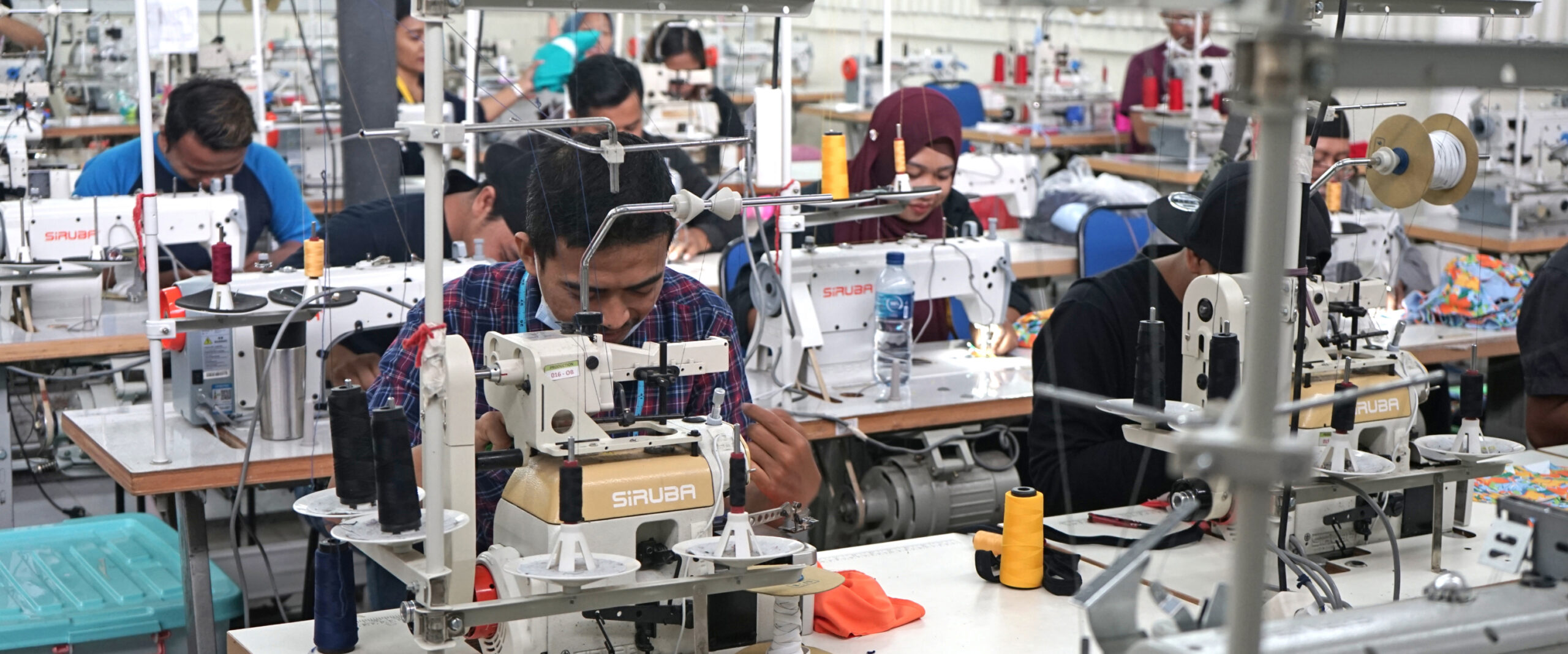 workers operating sewing machines in a modern garment manufacturing facility, producing swimwear